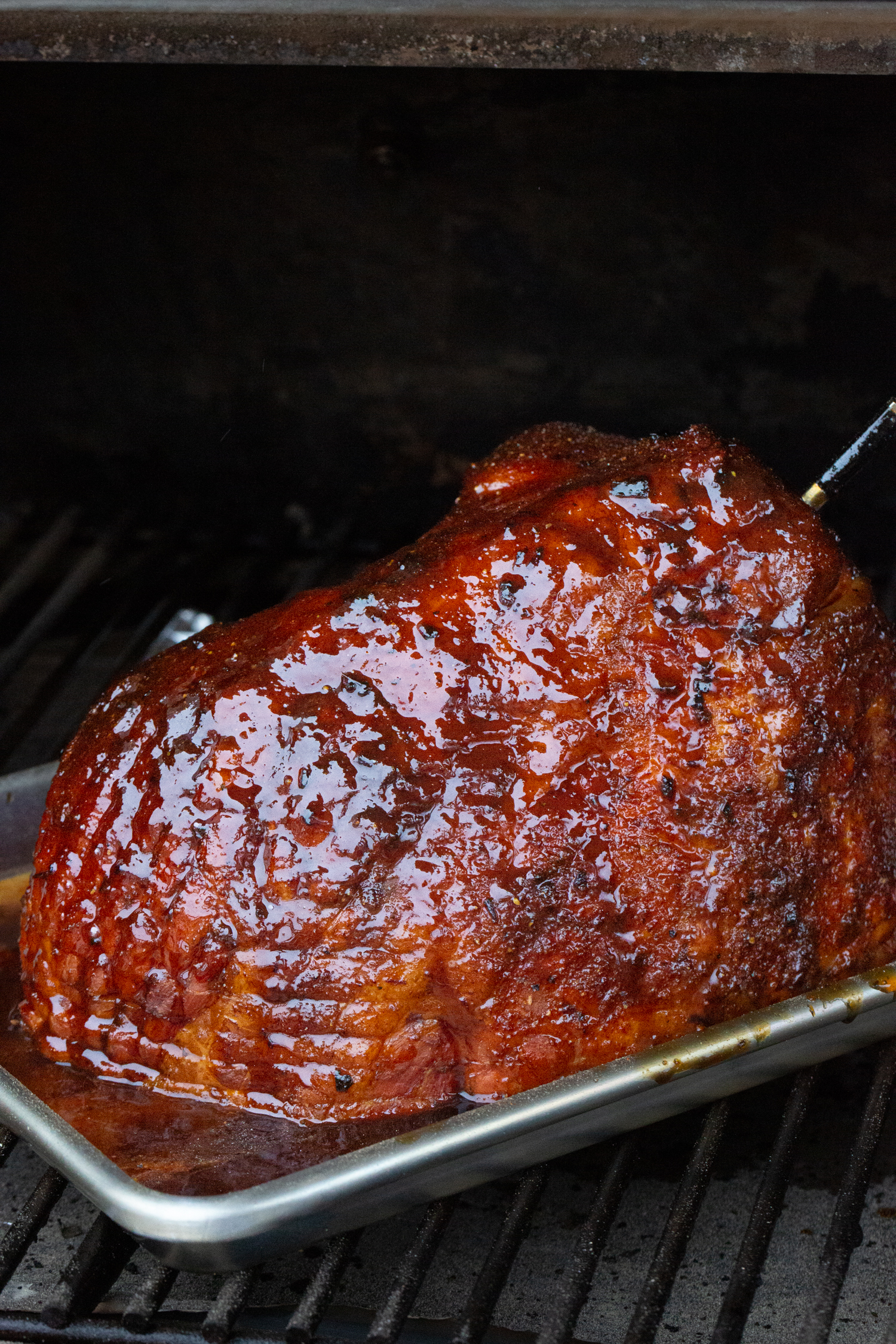 A smoked ham on a pellet smoker with bright red sauce and rub all over it.