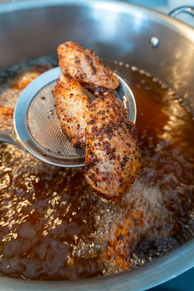 Chicken wings seasoned with dry rub being pulled from the deep fryer at a golden brown color.