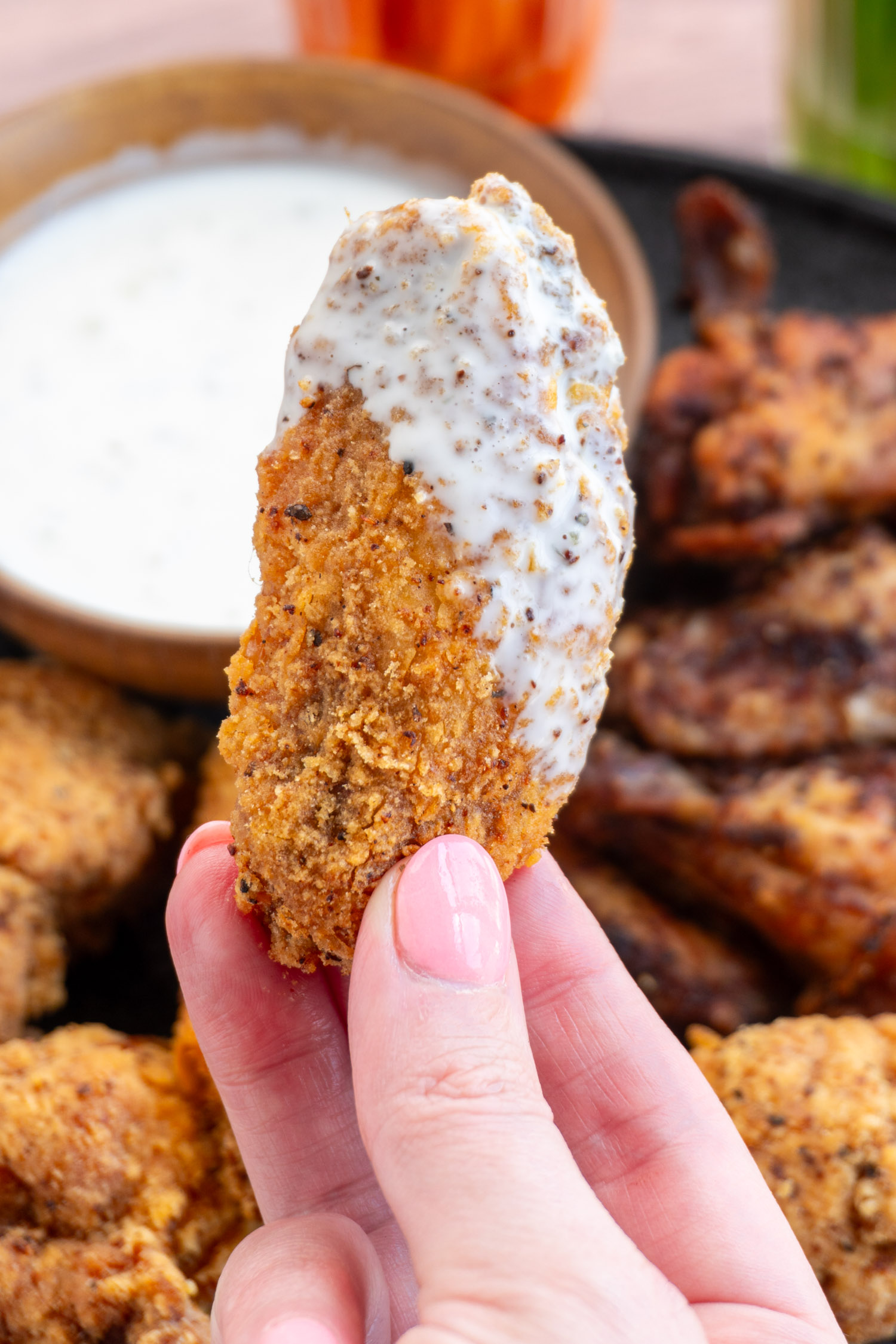 a crispy chicken wing up close, fried to golden brown and dipped in ranch dressing.