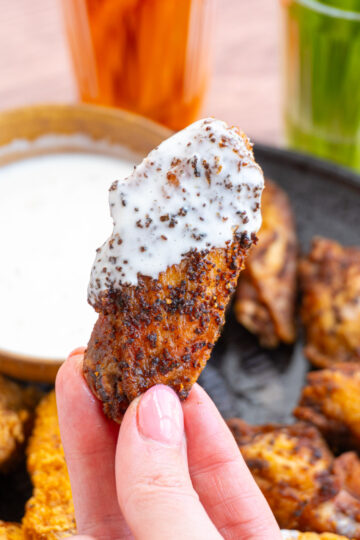 A close up of a fried chicken wing dipped in ranch and golden brown.