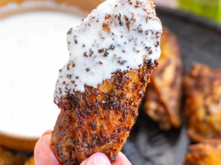 A close up of a fried chicken wing dipped in ranch and golden brown.