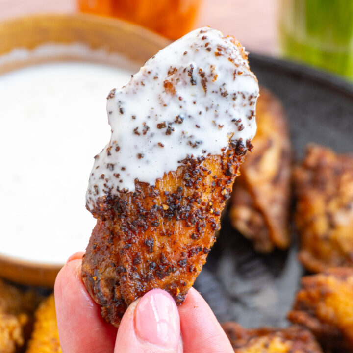 A close up of a fried chicken wing dipped in ranch and golden brown.