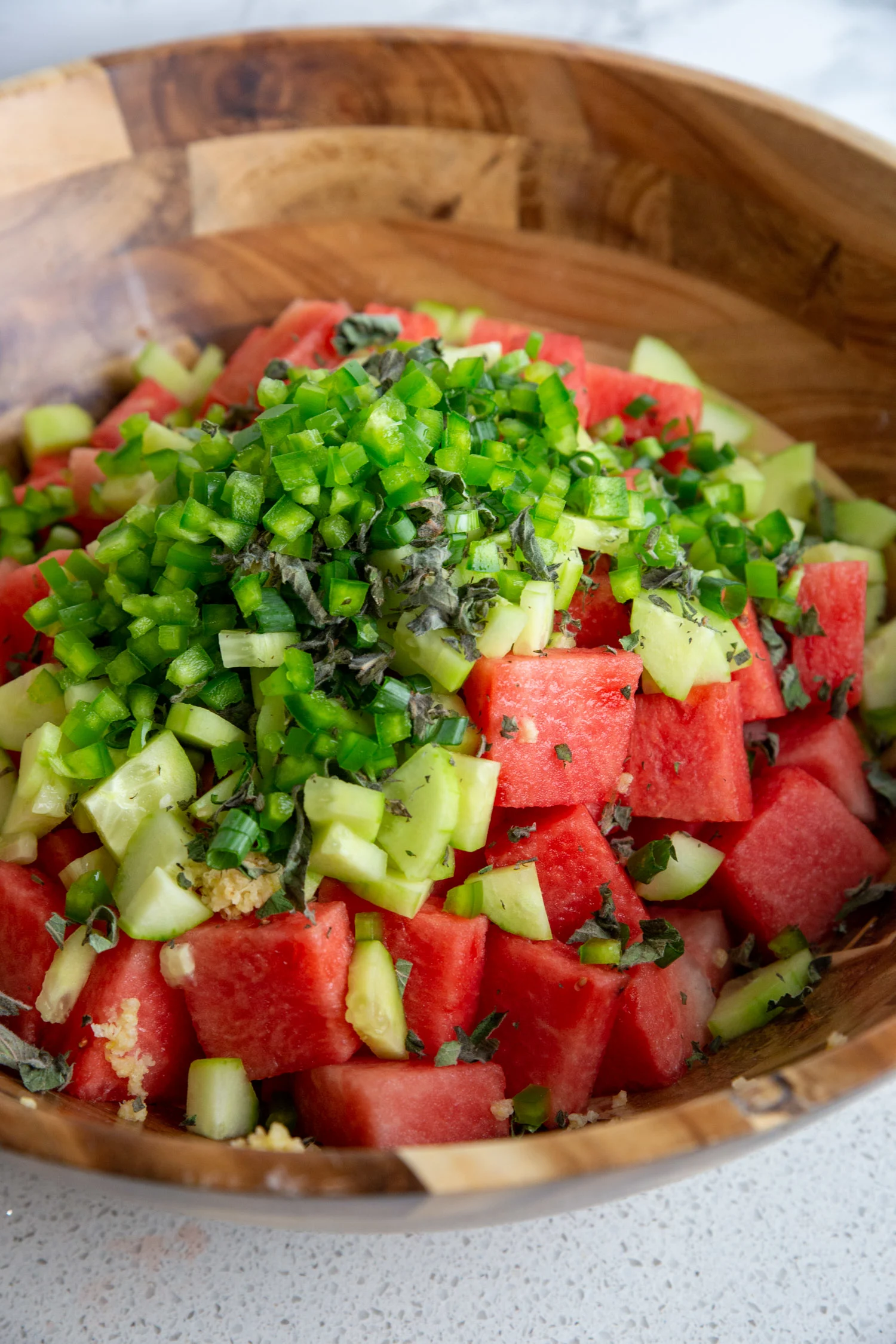 ingredients for a watermelon salad in a wooden bowl before being tossed.