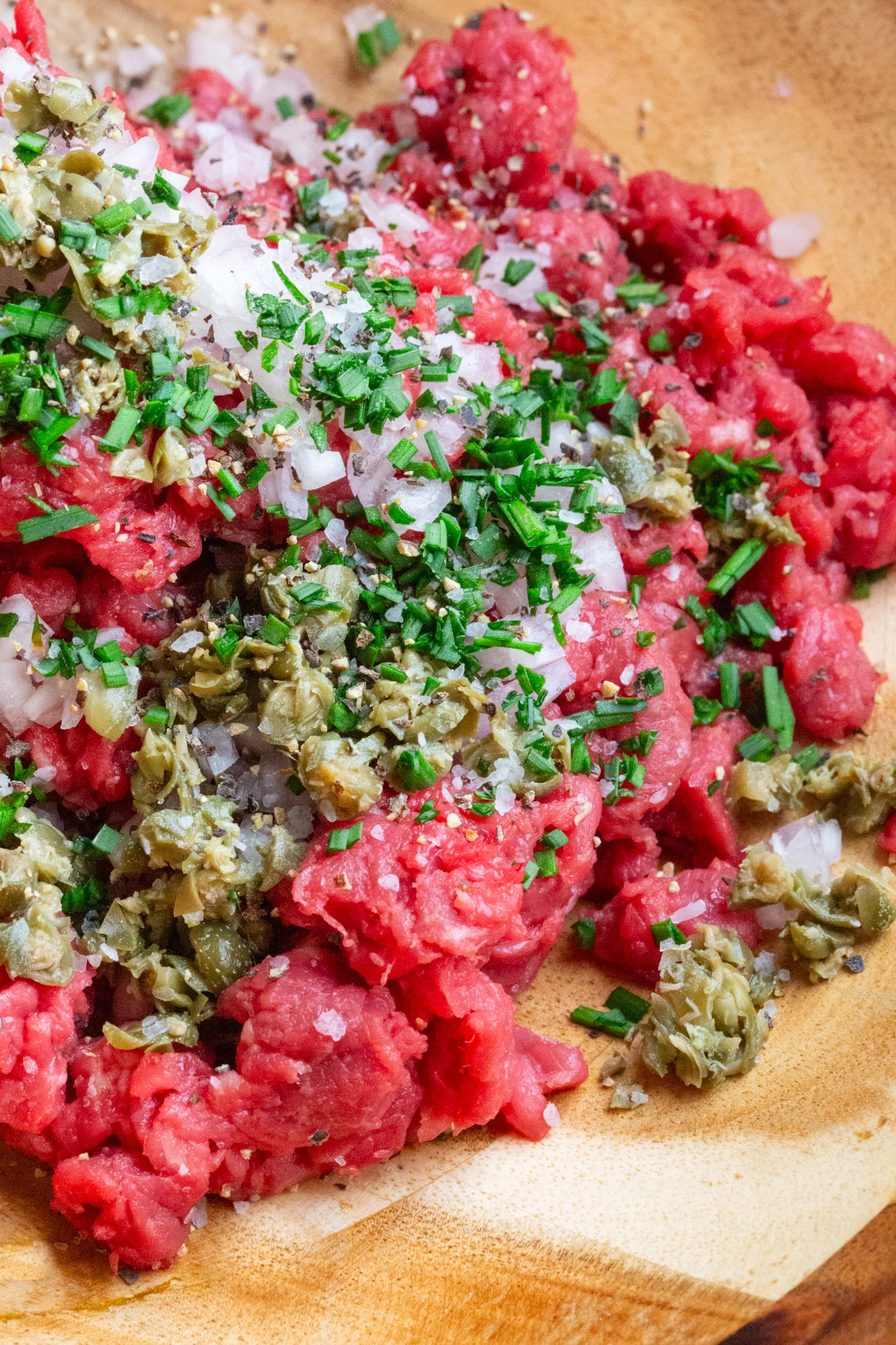 A bowl of beef tartare ingredients, chives, beef, seasonings.