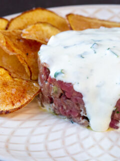 Beef Tartar covered in garlic aioli on a white plate with potato crisps.