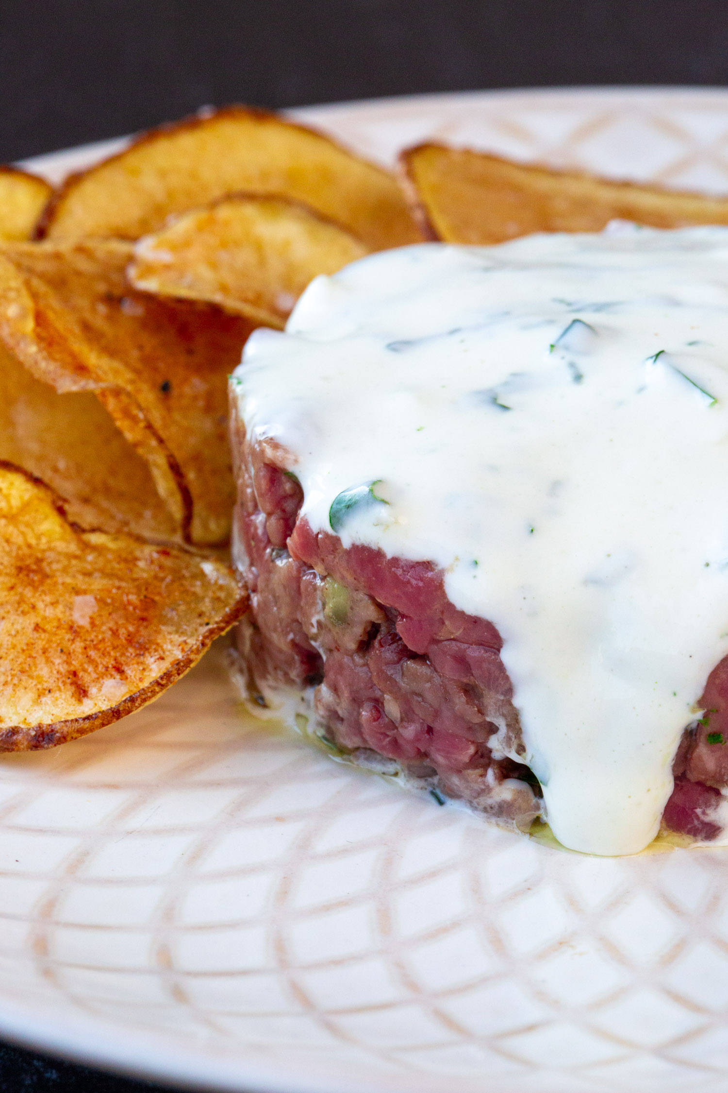 Beef Tartar covered in garlic aioli on a white plate with potato crisps.