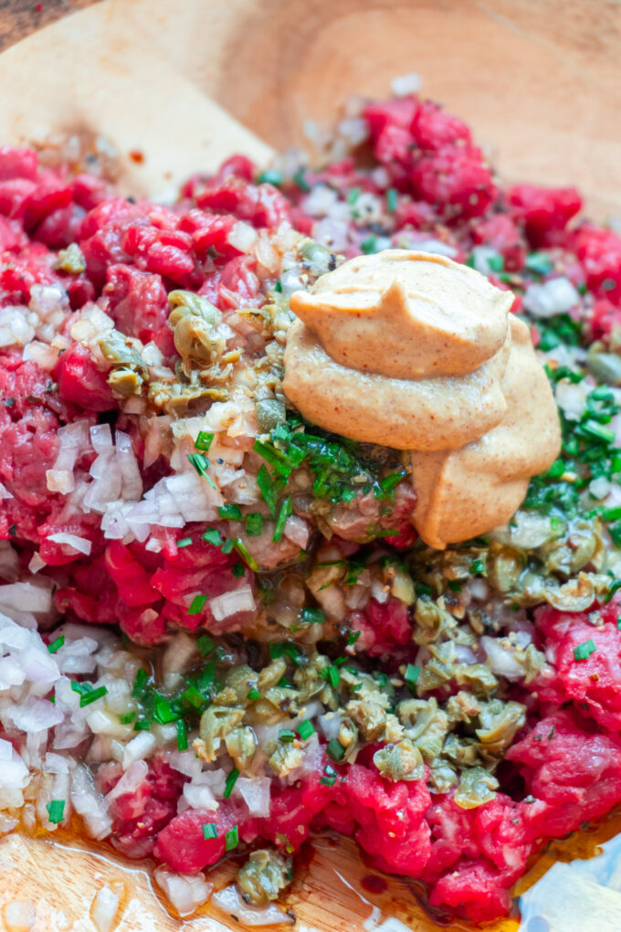 A bowl of beef tartare ingredients before being folded together, including raw beef tenderloin, mustard, shallot, herbs, and sauces.