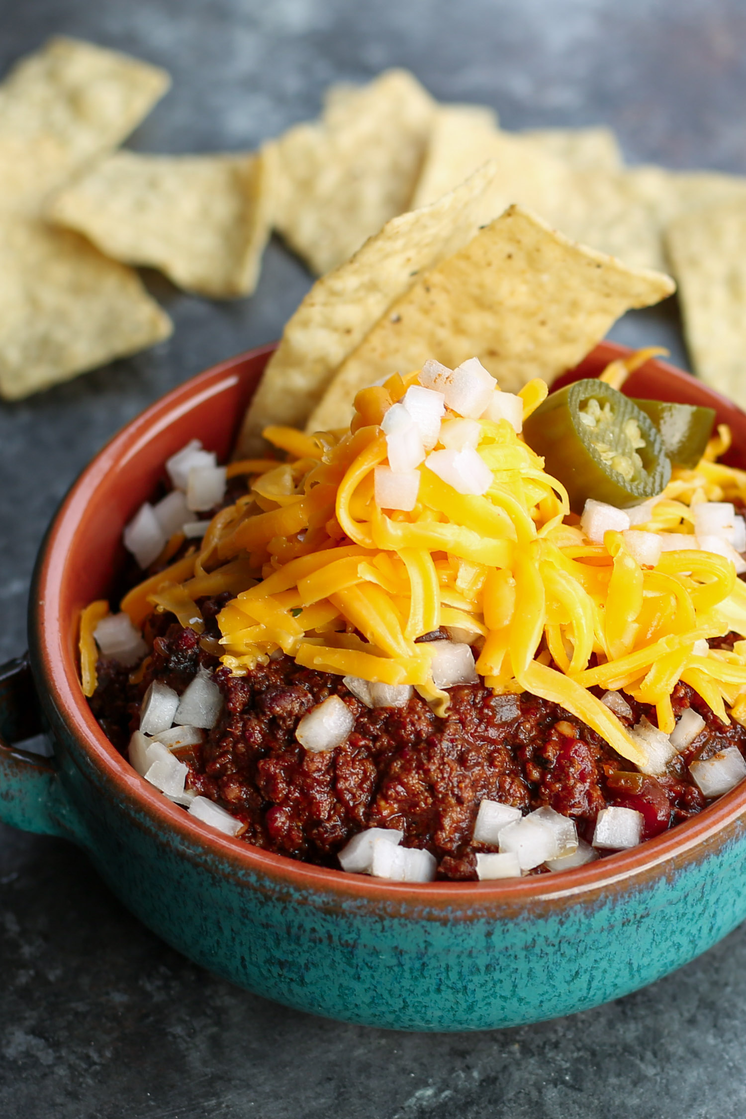 A bowl of bison chili topped with cheese and jalapeno peppers