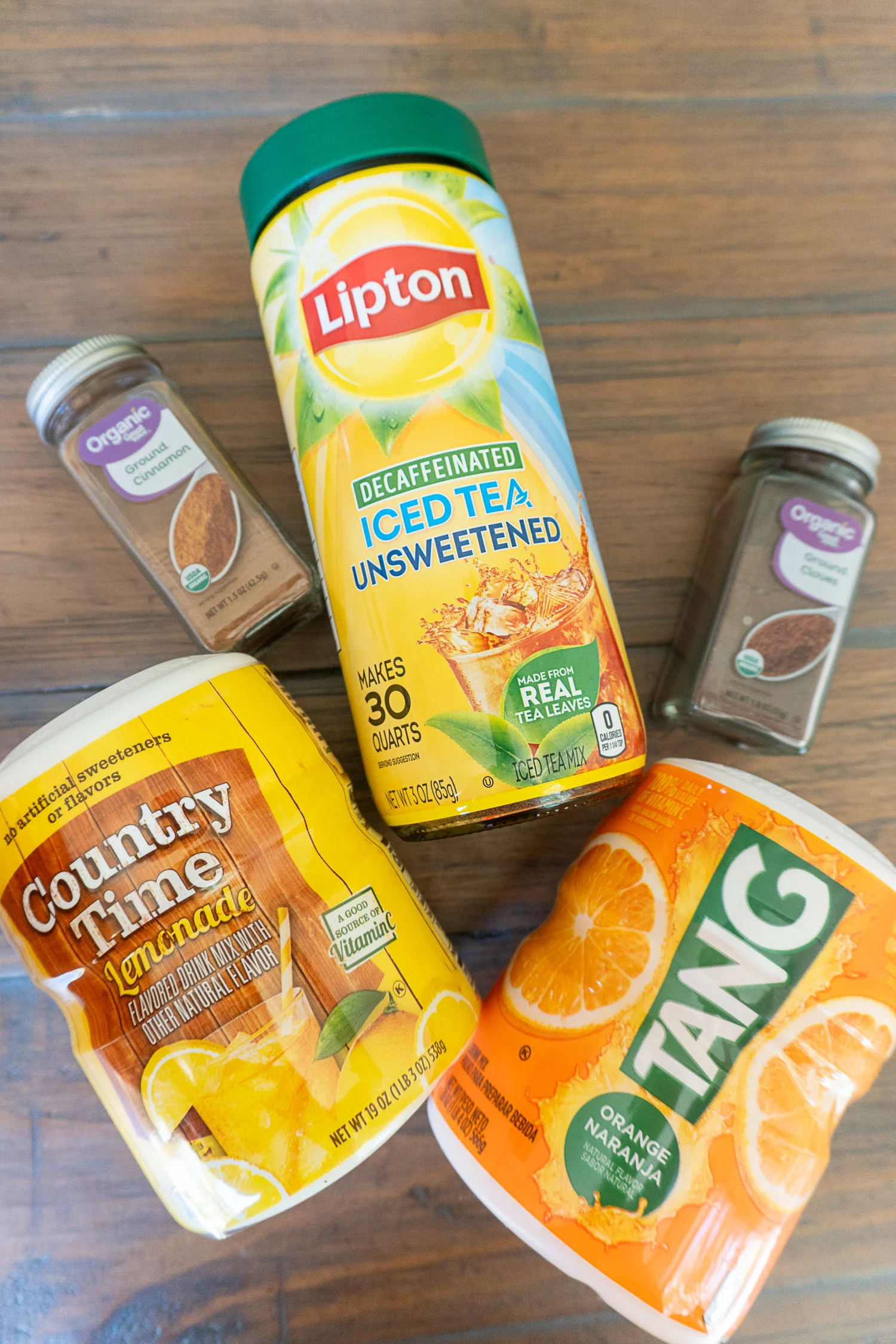 ingredients for friendship tea: dry lemonade mix, tang, tea mix, cinnamon, cloves on a wooden table