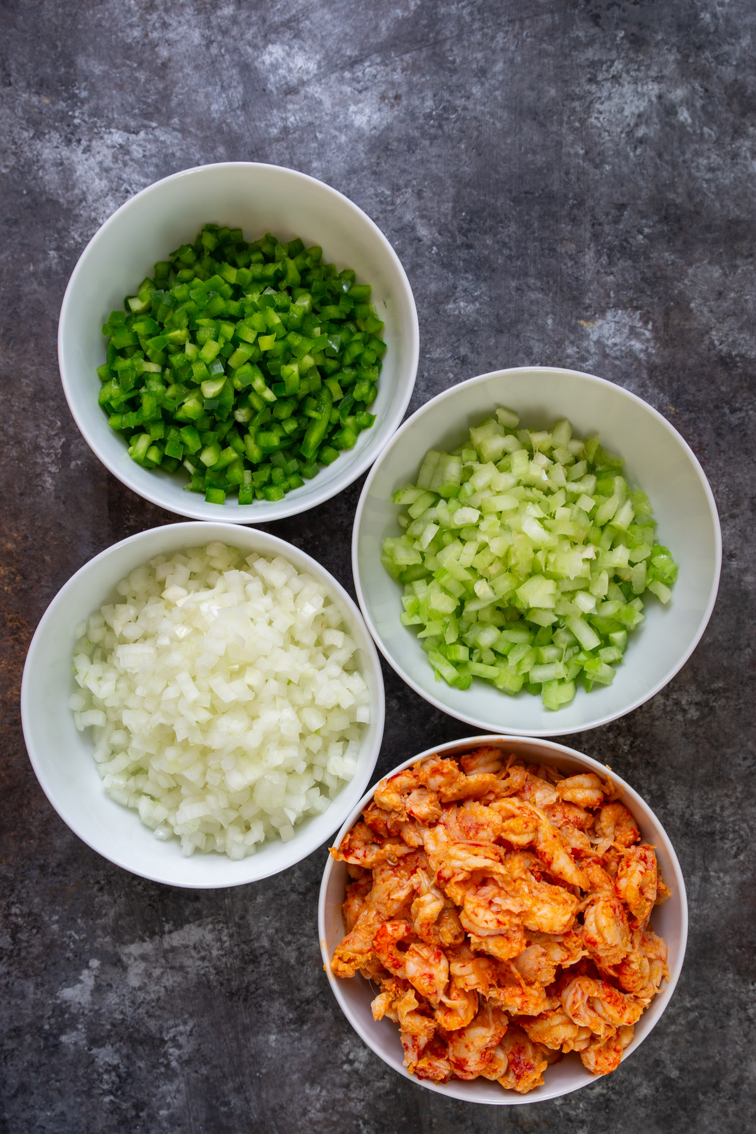Bowls of white onion, celery, green bell peppers, and cooked crawfish tails.