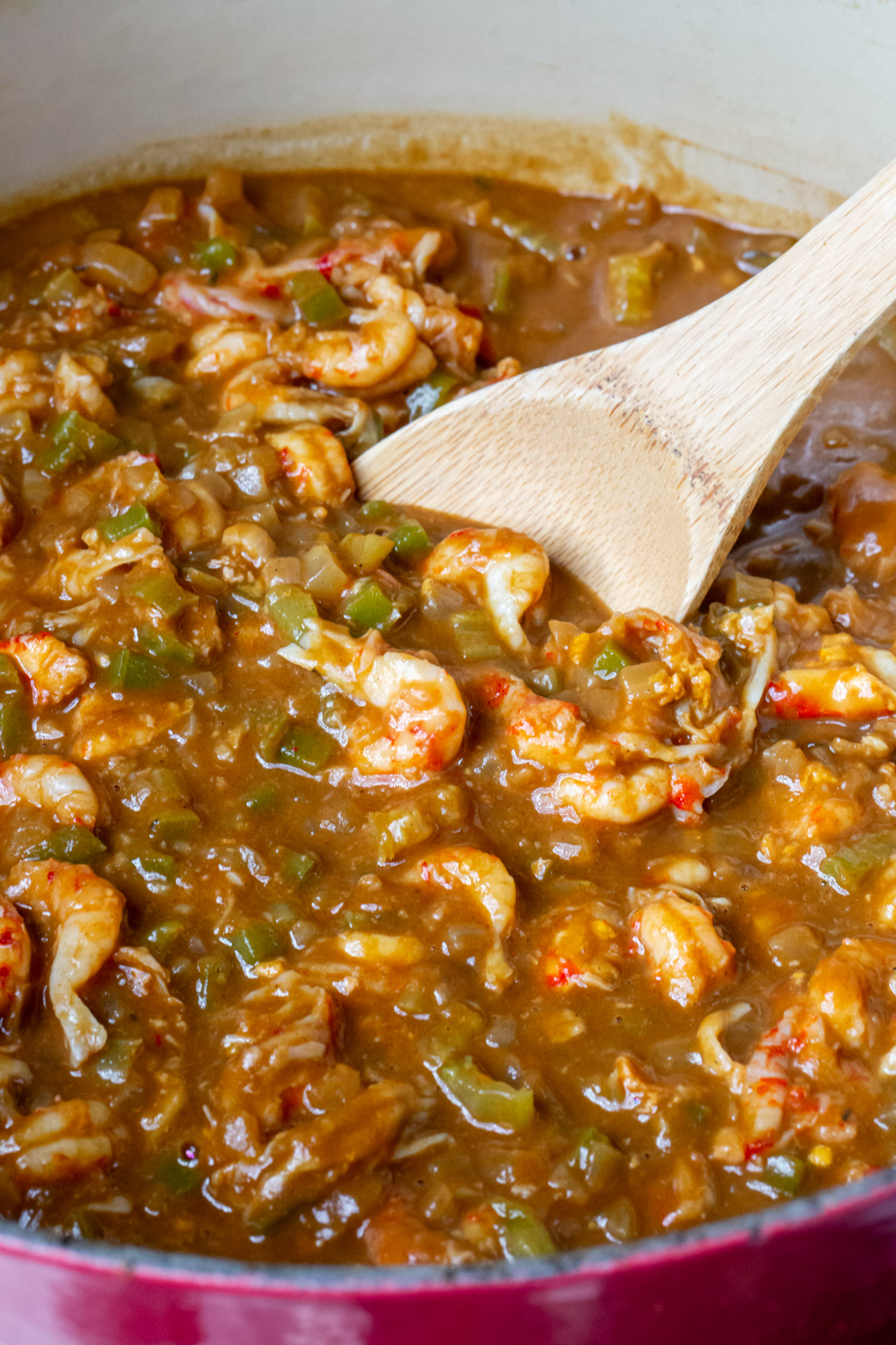 A big pot full of crawfish etoufee simmering in brown gravy with a wooden spoon.