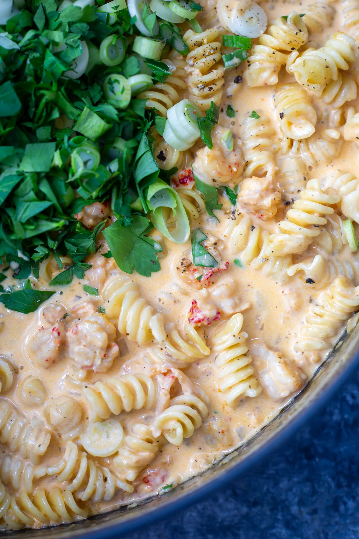 a close up of a pot full of creamy sauce, juicy crawfish tails, and rotini pasta.