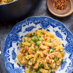 A crawfish pasta on a blue plate with fresh green herbs.