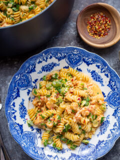 A crawfish pasta on a blue plate with fresh green herbs.
