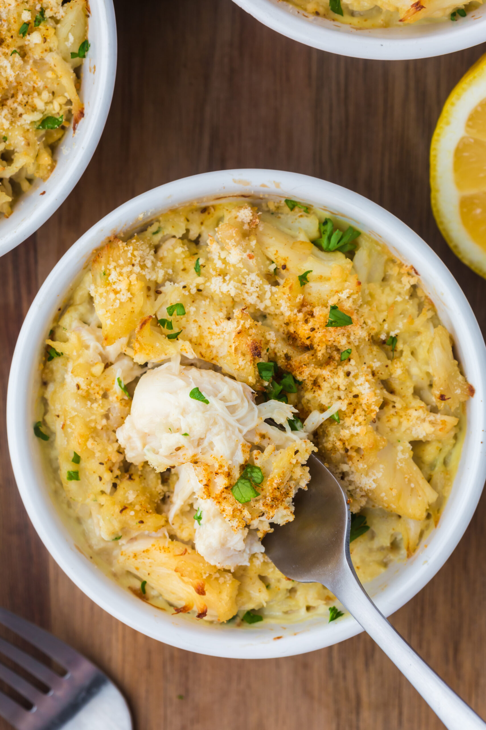 a overhead shot of a ramekin filled with baked crab imperial, a fork is scooping up a bite of the crab imperial