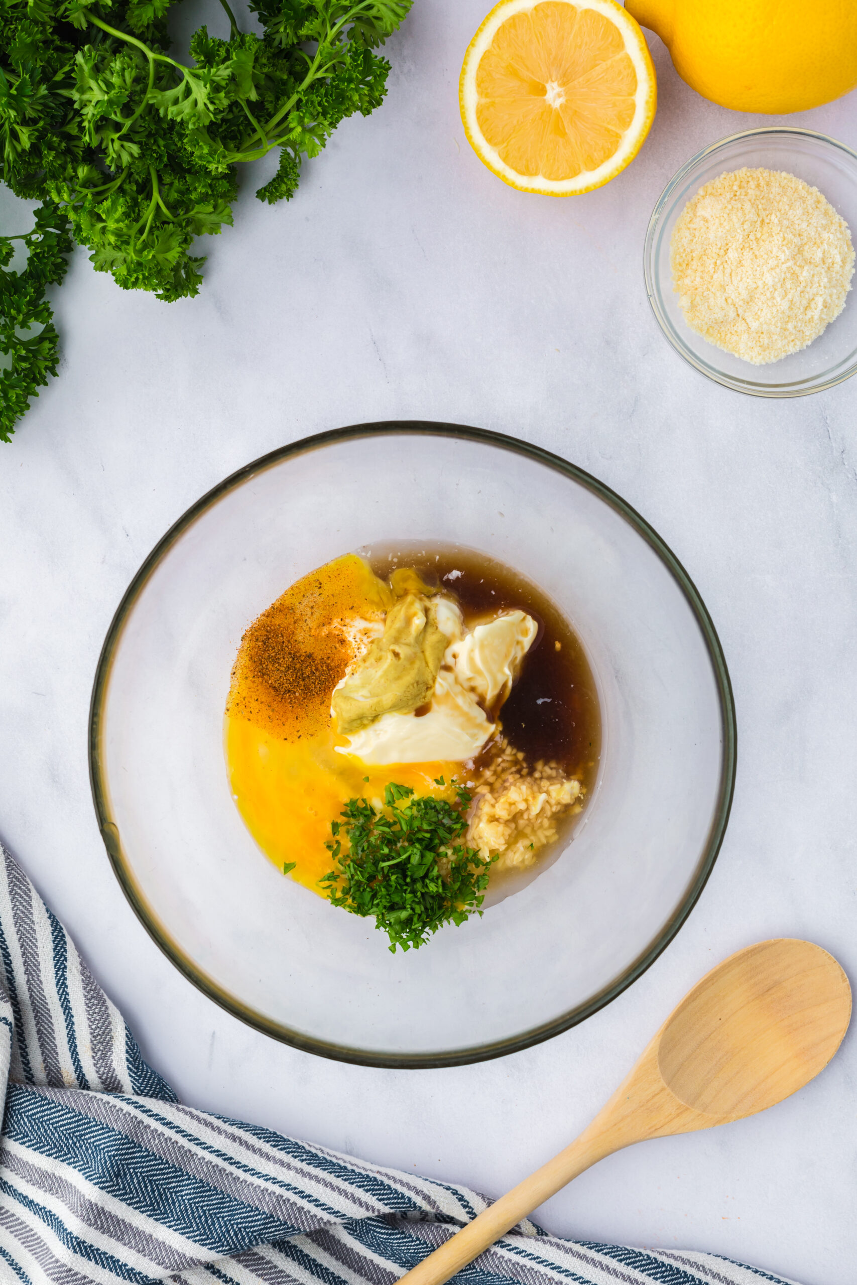 glass bowl on a table filled with imperial sauce ingredients (egg, mayonnaise, mustard, Worcestershire sauce, Old Bay seasoning, and Lemon Juice)
