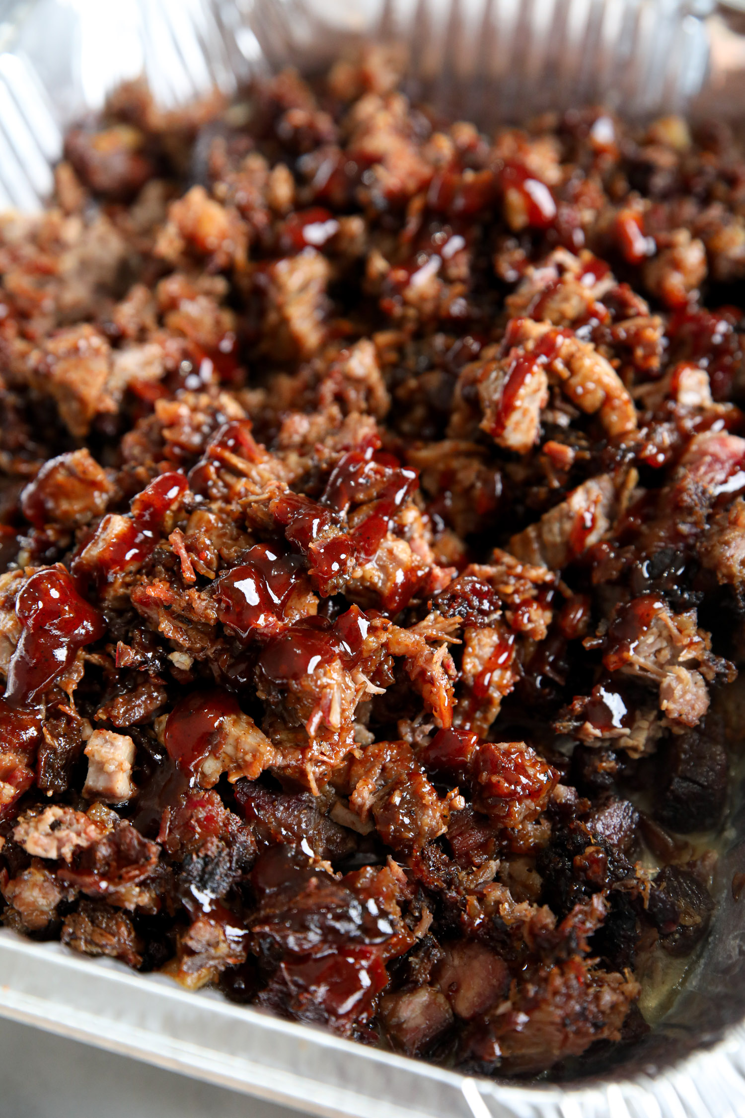 An aluminum pan of chopped brisket that has been drizzled with barbecue sauce