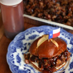 Brisket Sandwich with a Texas flag toothpick stuck into the bun, on top of a blue decorative plate