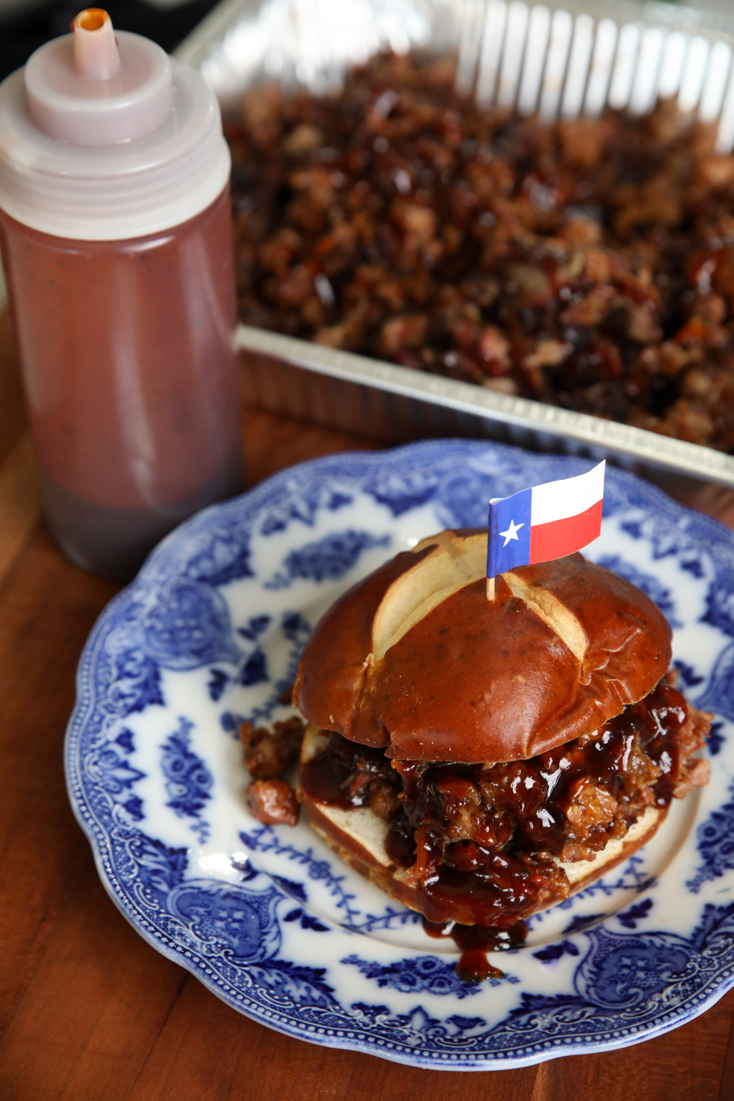 Brisket Sandwich with a Texas flag toothpick stuck into the bun, on top of a blue decorative plate