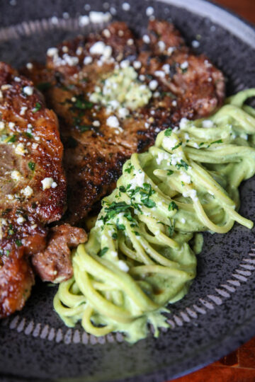 A plate of creamy green spaghetti with steaks on a black plate