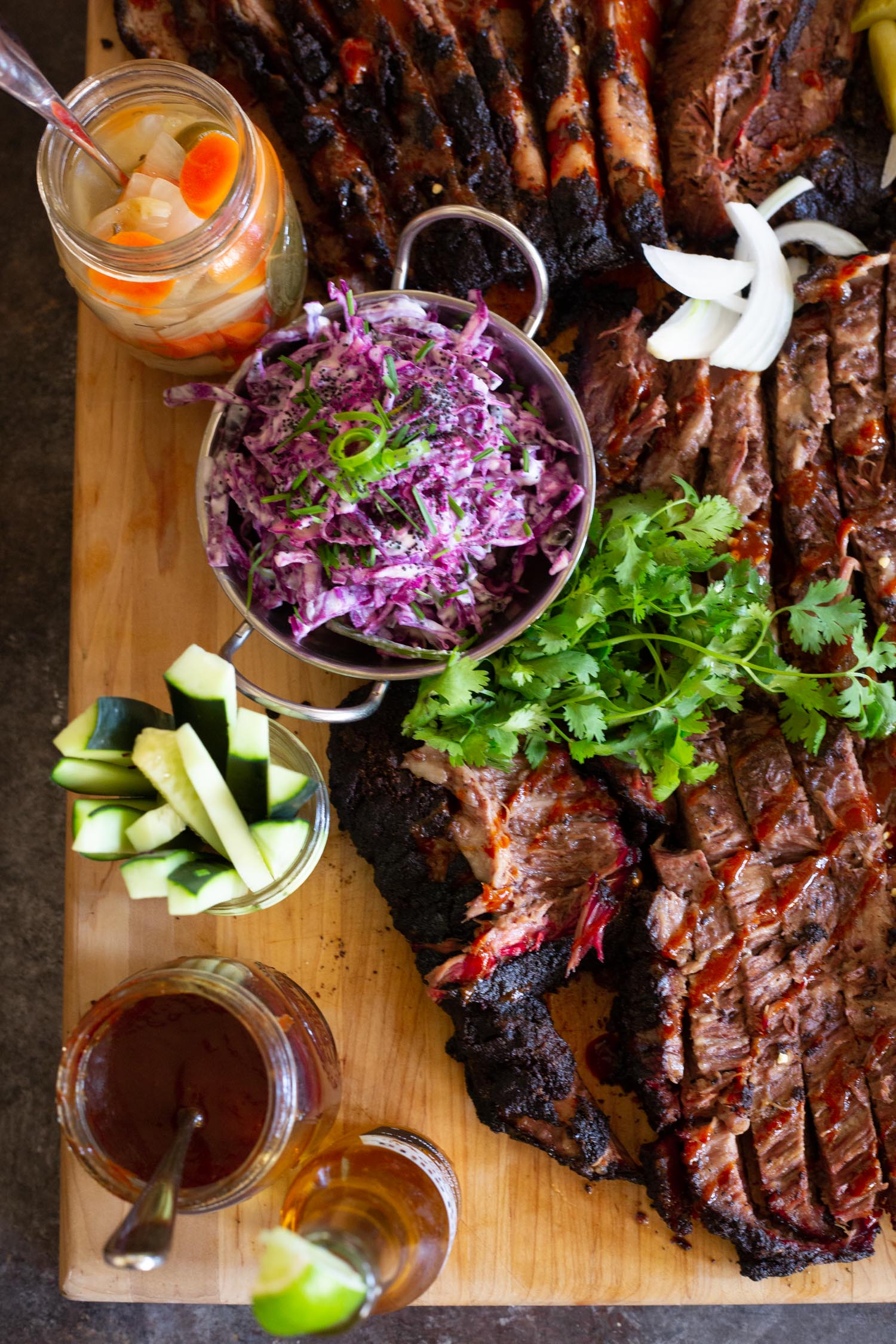 an assortment of different toppings and ingredients in jars next to a fully cooked and cut brisket