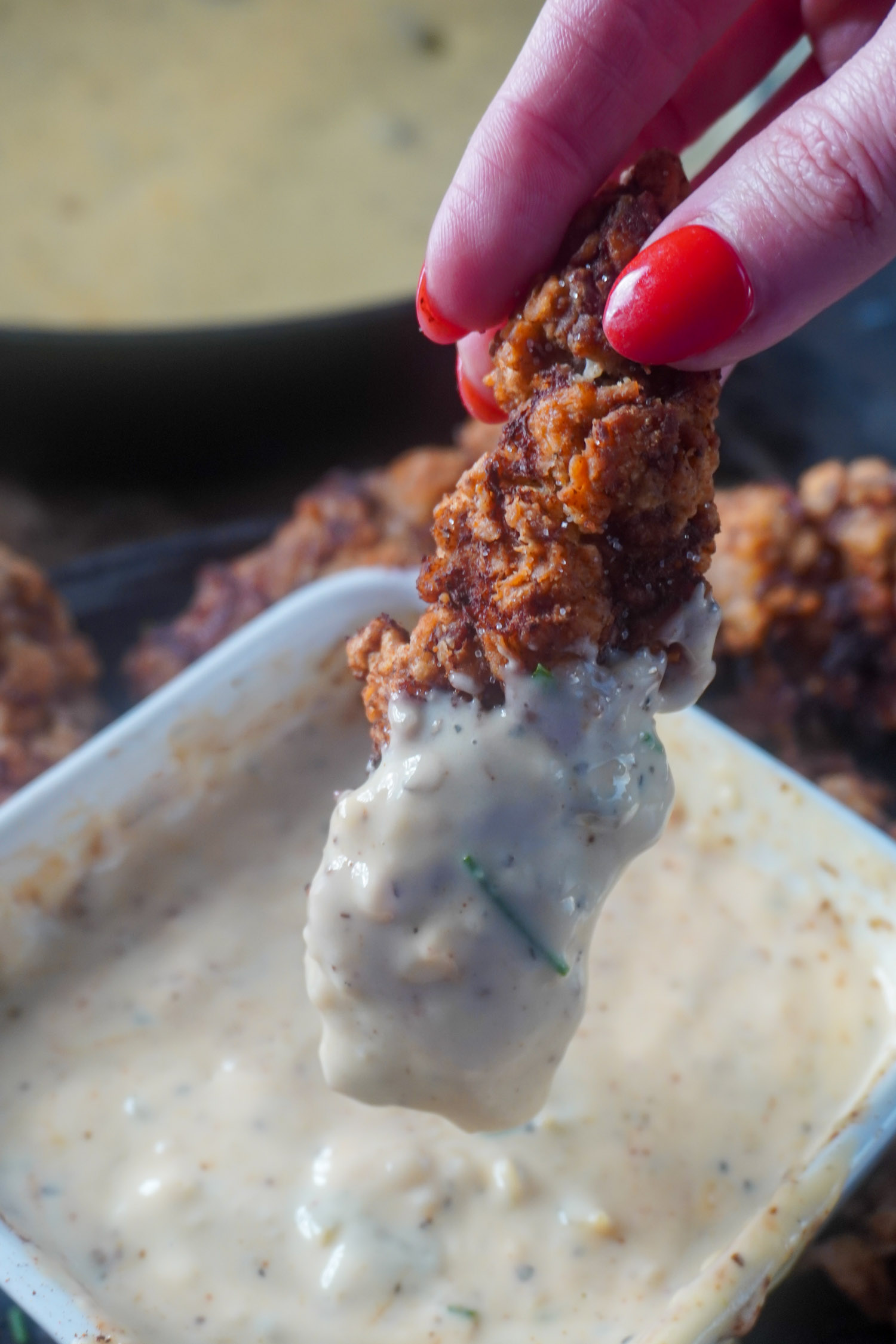 a steak finger being removed rom a pot of gravy