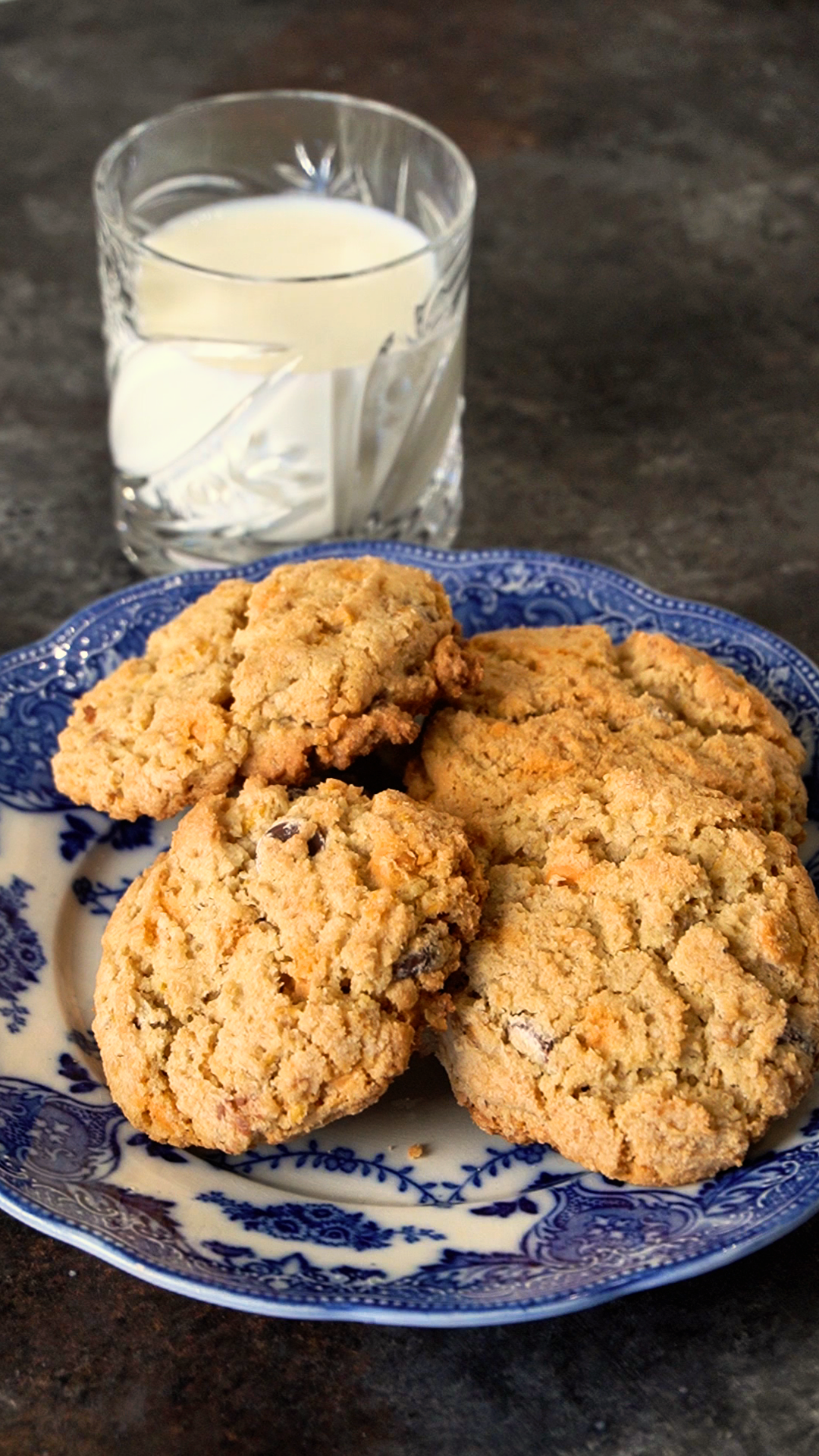 a pile of cooked cowboy cookies sitting on a decorative plate with a glass of milk in the background
