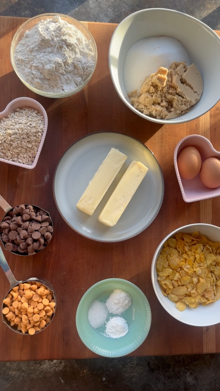 all ingredients for cowboy cookies in separate bowls sitting on a wooden slab