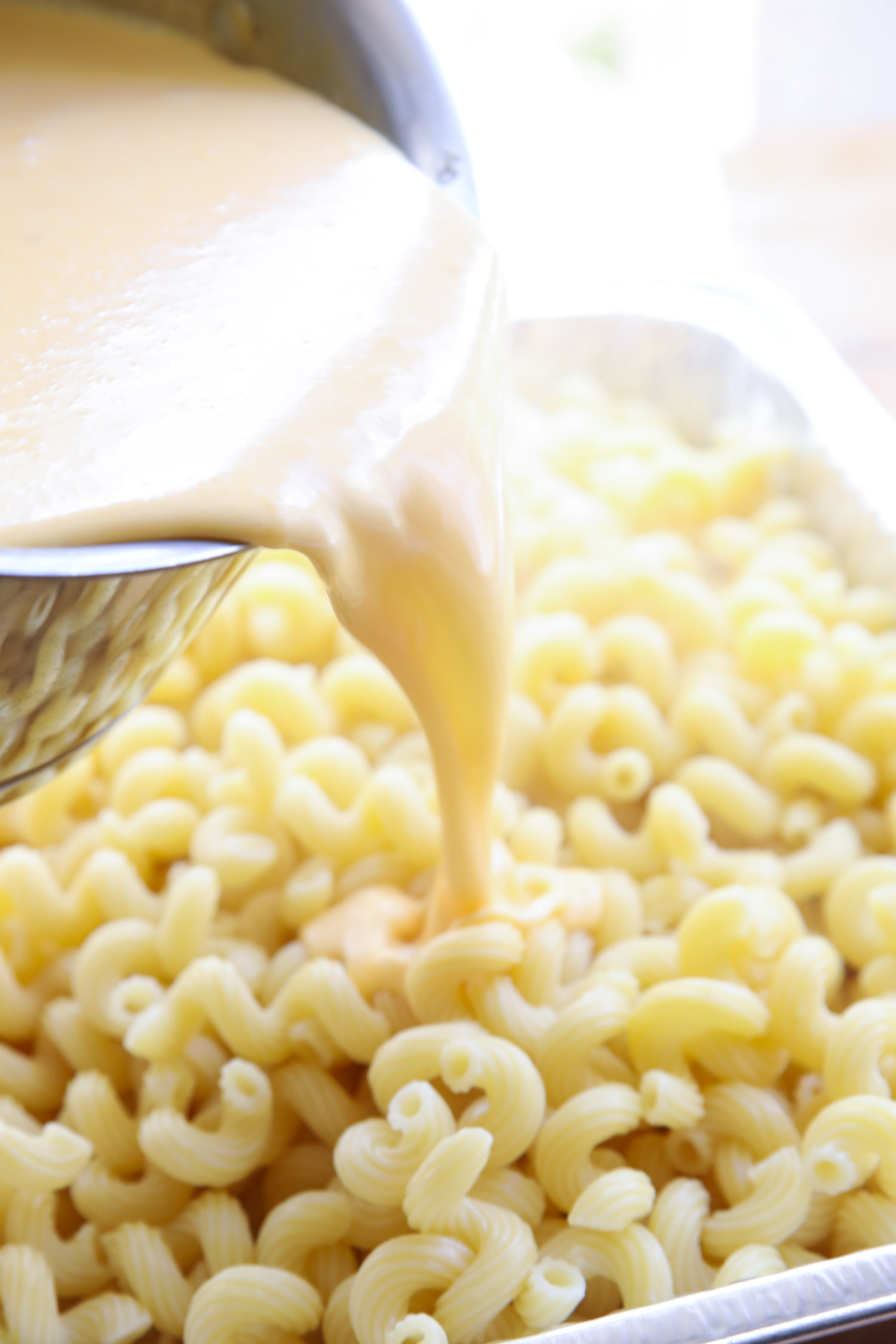 cream being poured into a pan of cooked macaroni noodles