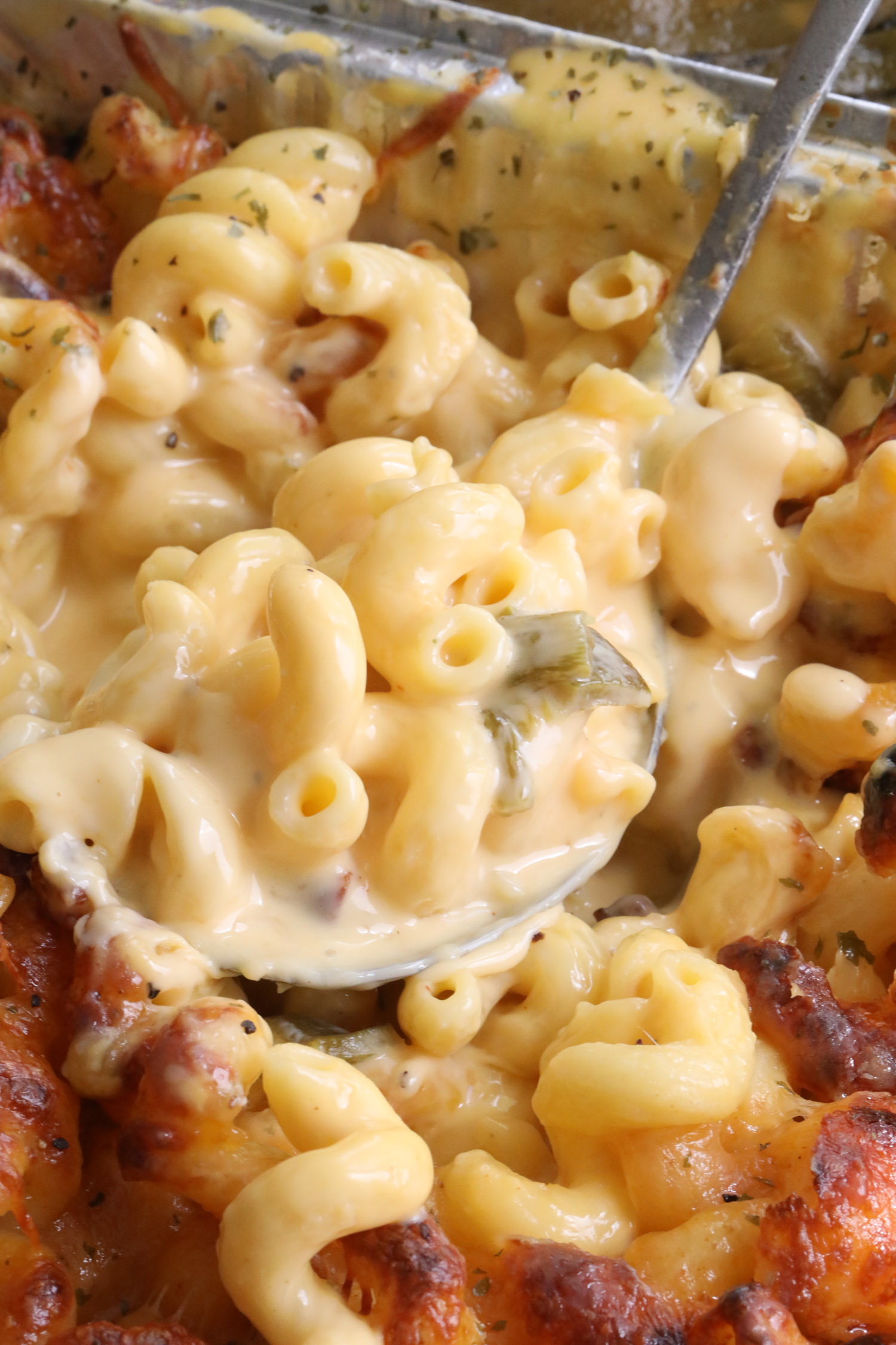 creamy green chile mac and cheese in a serving platter with a spoon scooping up a bite-sized portion