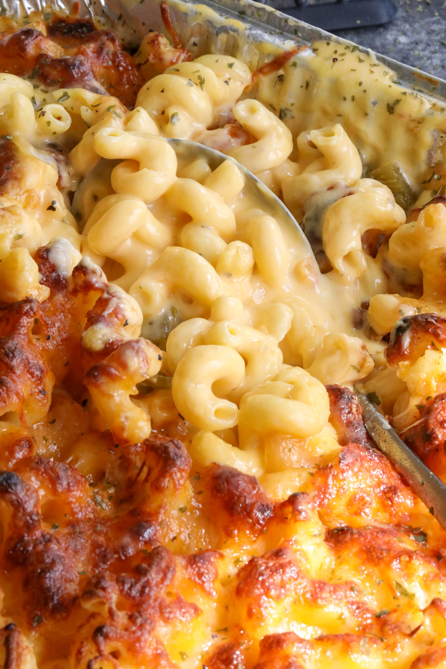 cooked green chile mac and cheese in a serving platter with a spoon dipping into the mac and cheese