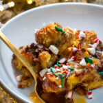 A bowl of peppermint bark bread pudding with a gold spoon in front of the christmas tree.