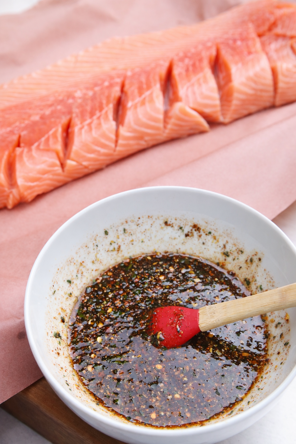 a bowl of maple glaze containing orange zest and herbs, scored side of salmon in background