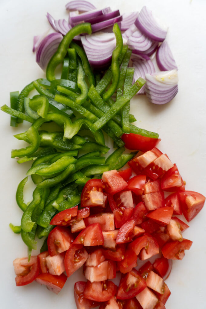 A cutting board full of bell pepper, chopped tomatoes, and slices of red onion.