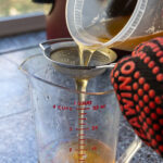 Pouring fresh rendered tallow from brisket trimmings through a sieve and into a quart jar.