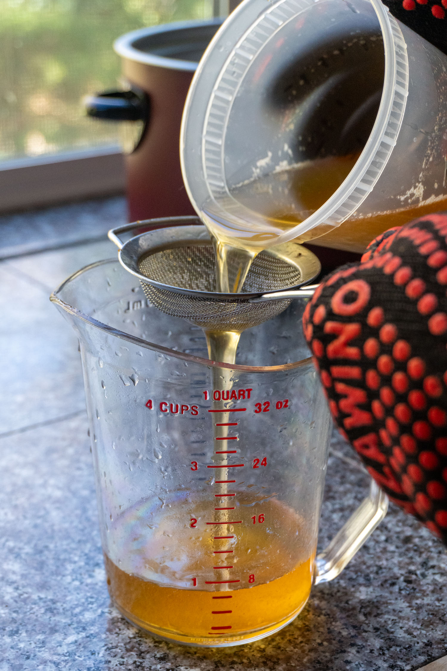 Pouring fresh homemade tallow through a sieve and into a holding container.