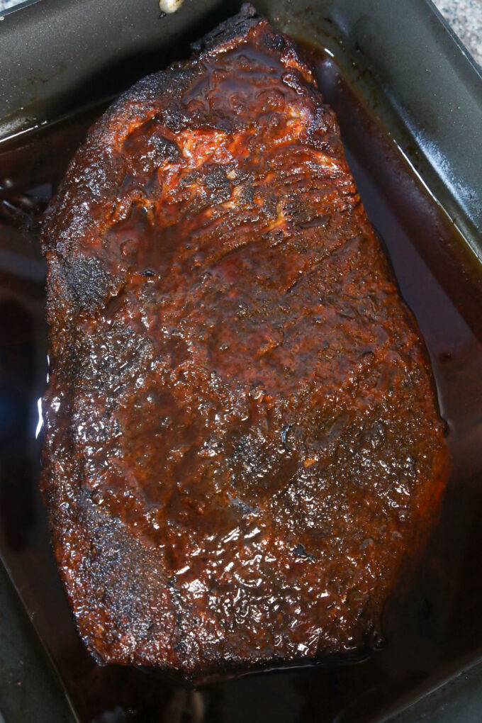 Whole brisket in sauces resting in a large roasting pan.