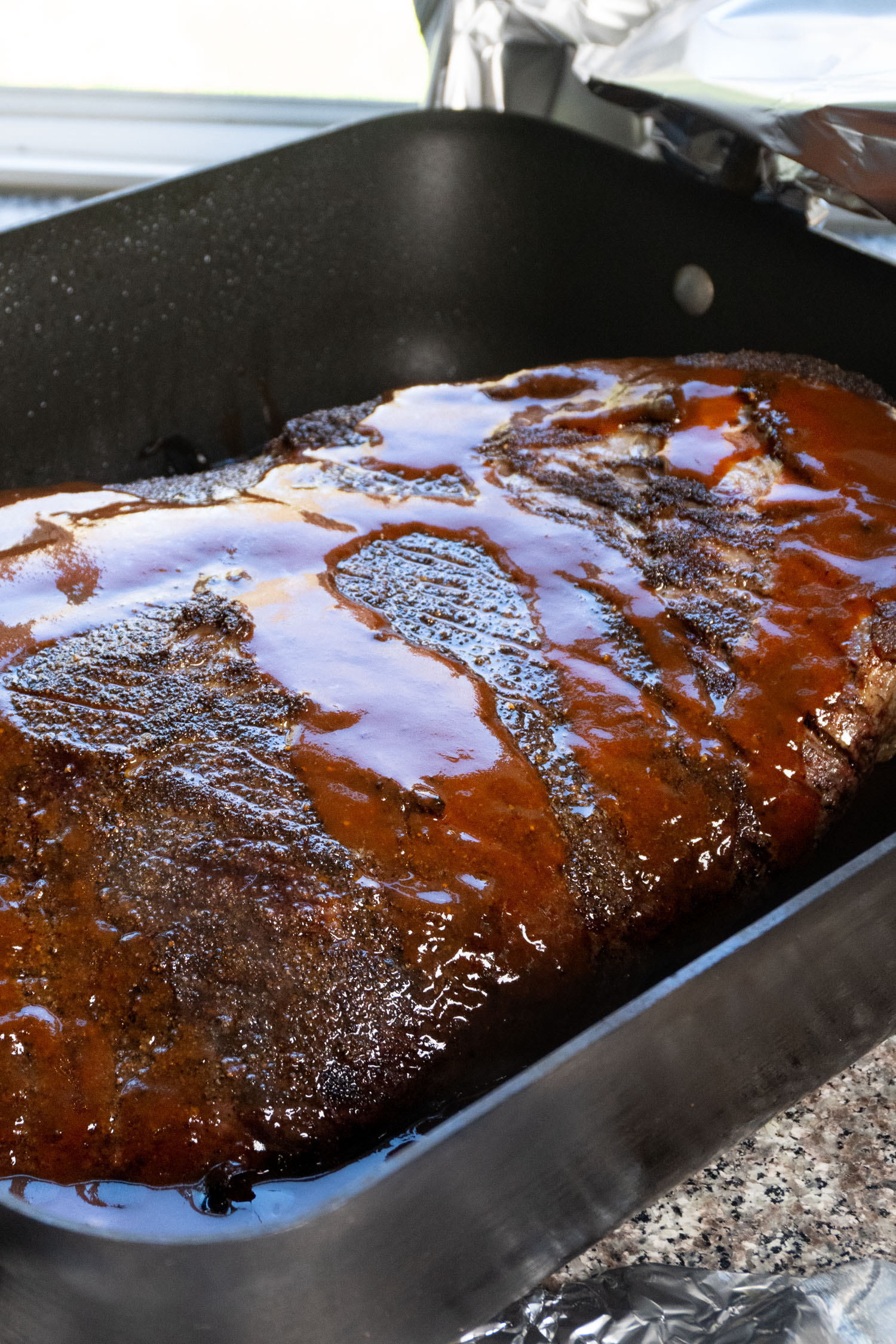 A roasting pan full of a whole packer brisket smothered in barbecue sauce.