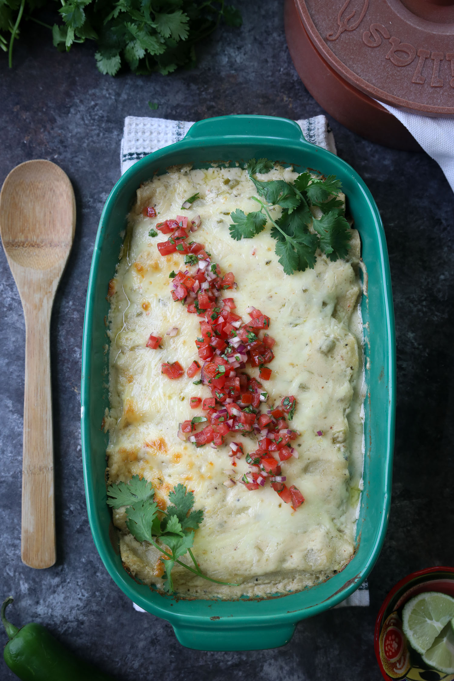 A casserole dish of brisket enchiladas from above, they are surrounded by various ingredients used to make the dish.