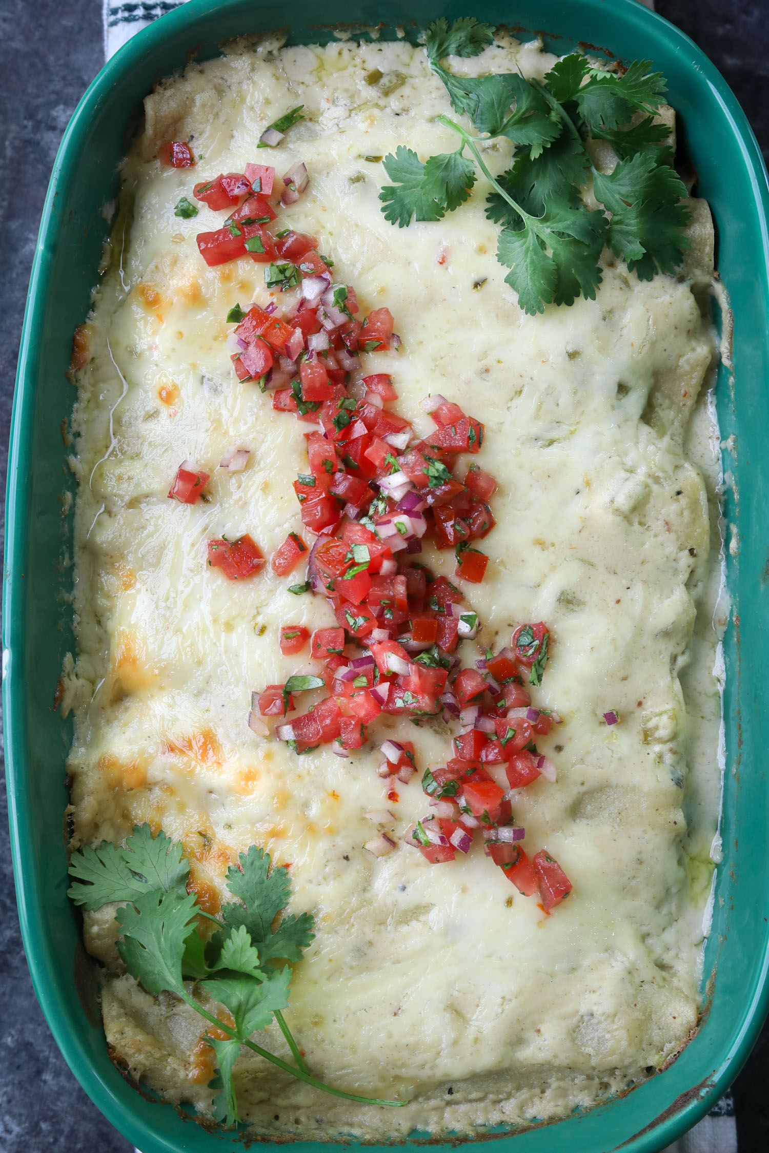 A full casserole dish of baked enchiladas perfectly cooked and topped with vibrant pico de gallo