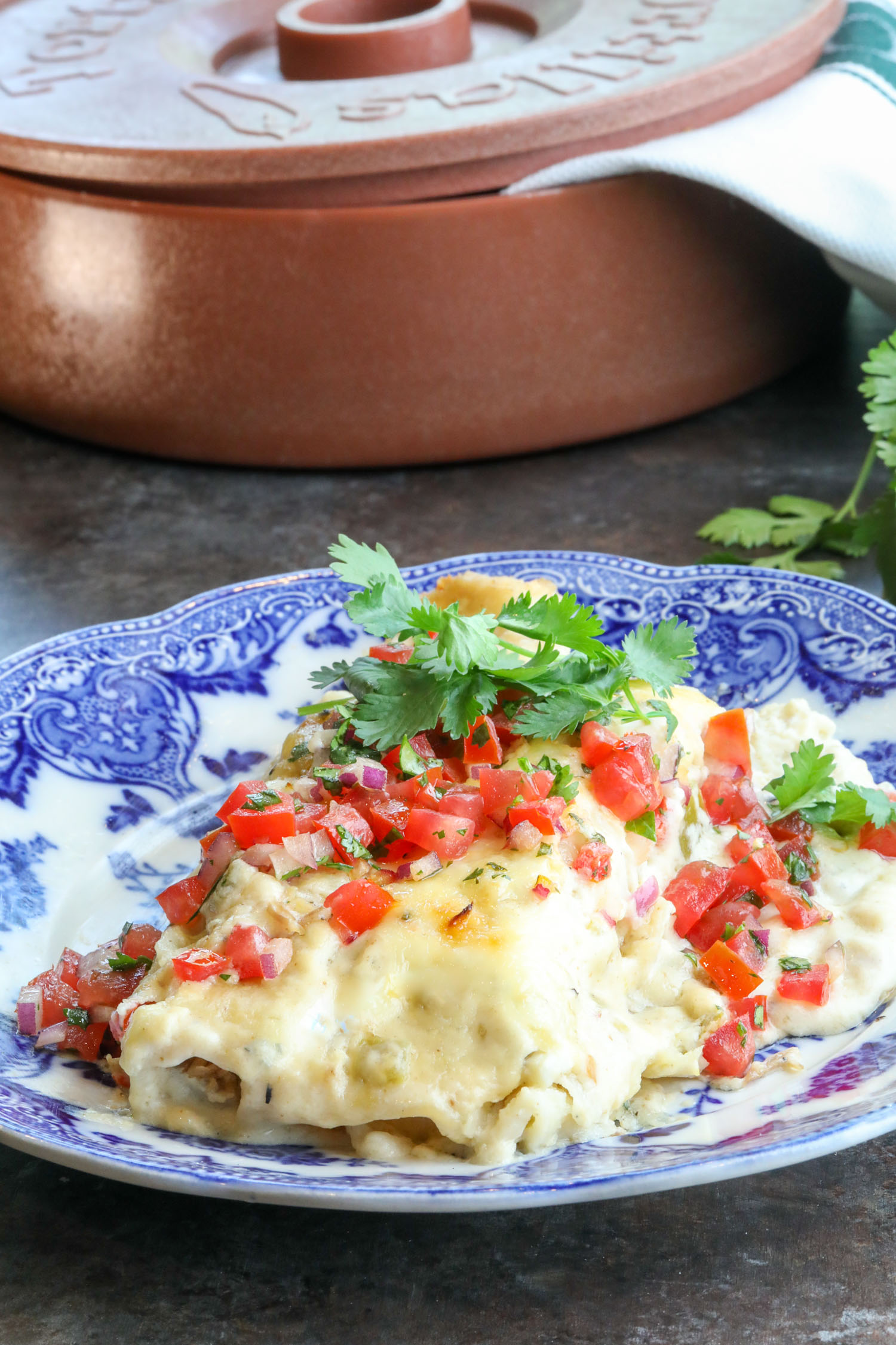 A blue plate full of a portion of brisket enchiladas with cilantro and pico de gallo on top.