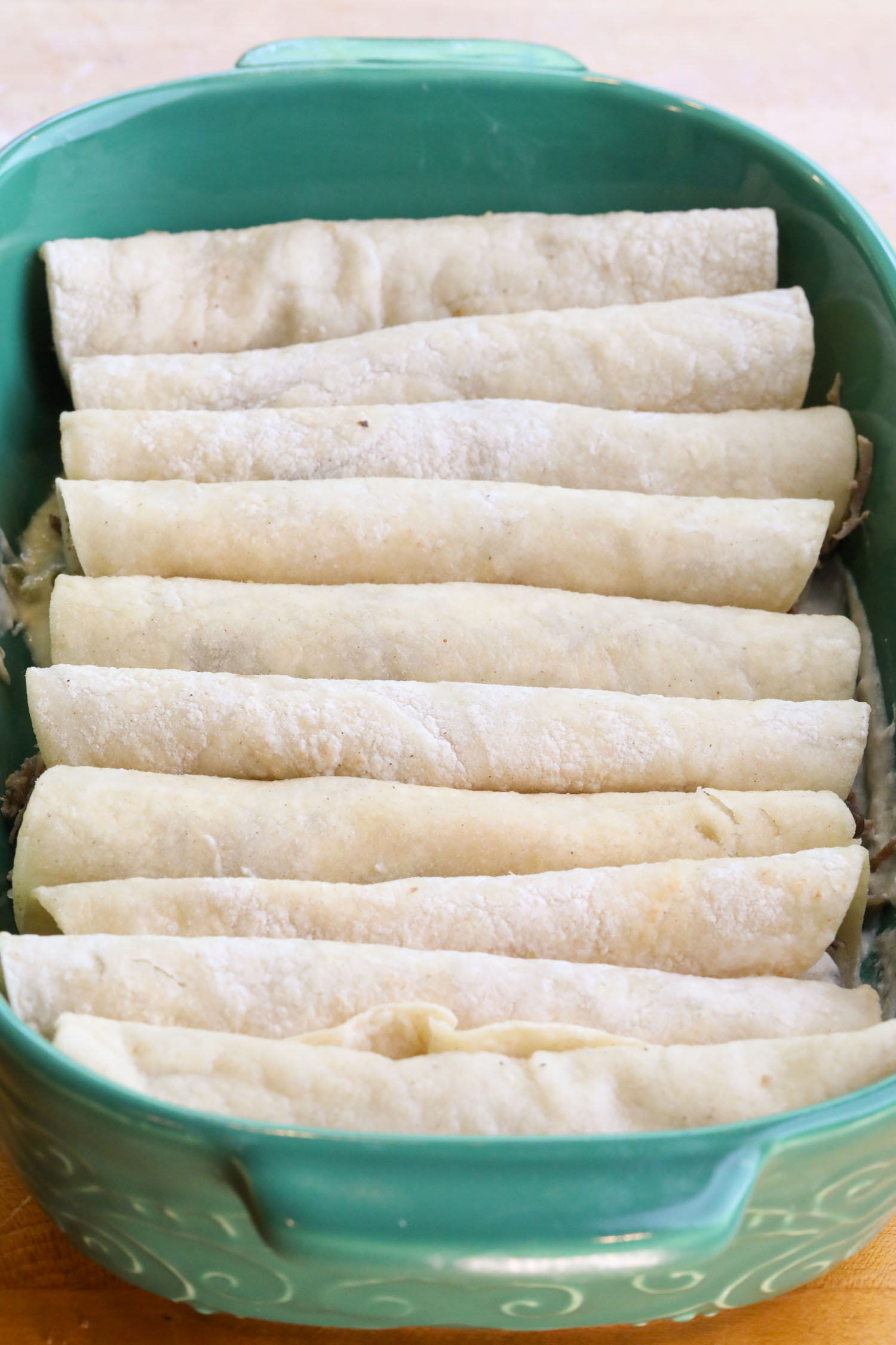 a casserole dish full of rolled enchiladas, awaiting the sauce