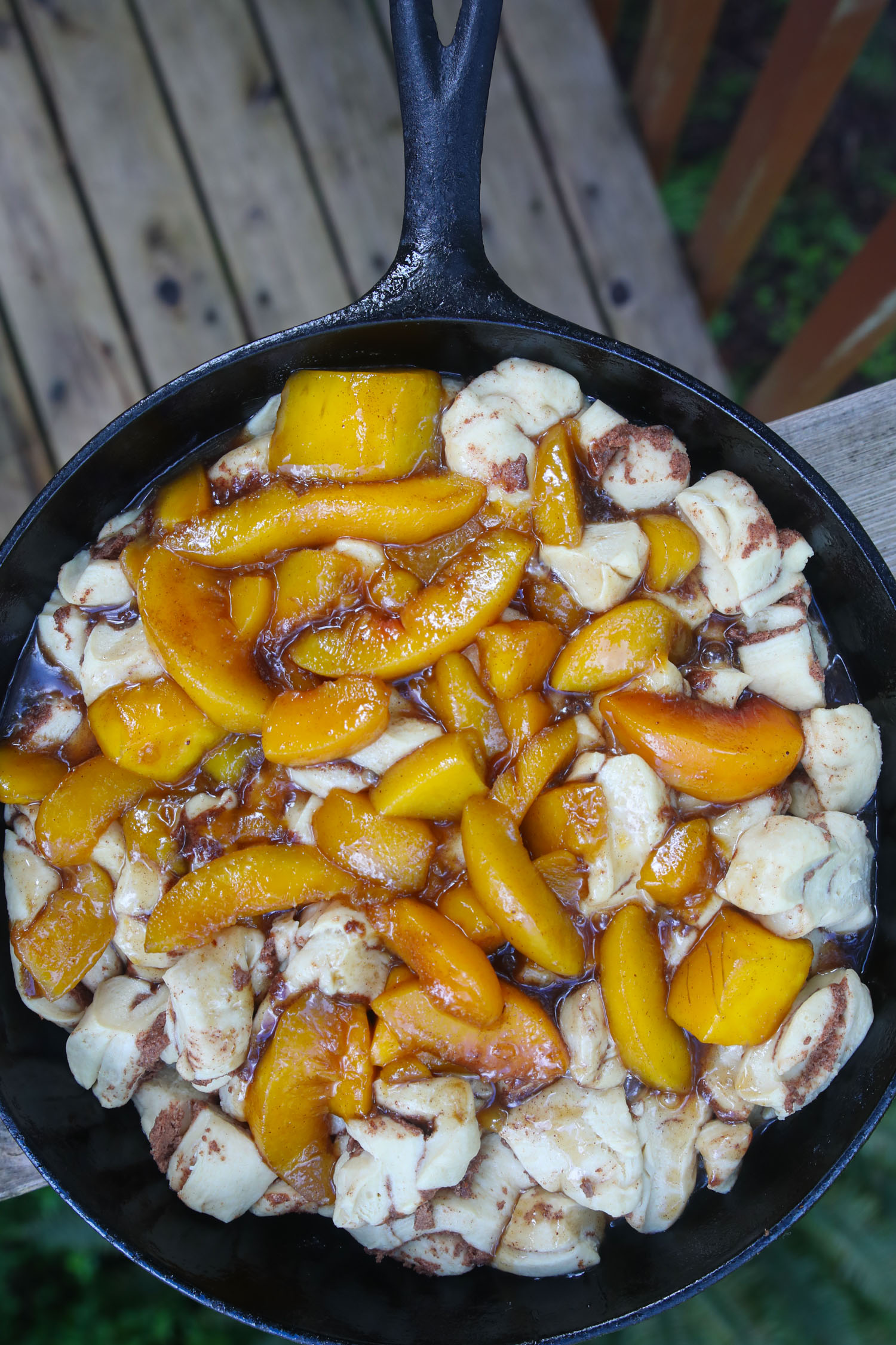 A cast iron skillet containing snippets of cinnamon rolls and topped with the homemade peach topping.