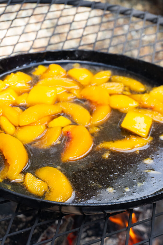 frozen peaches in a watery mixture in a cast iron pan over a fire.