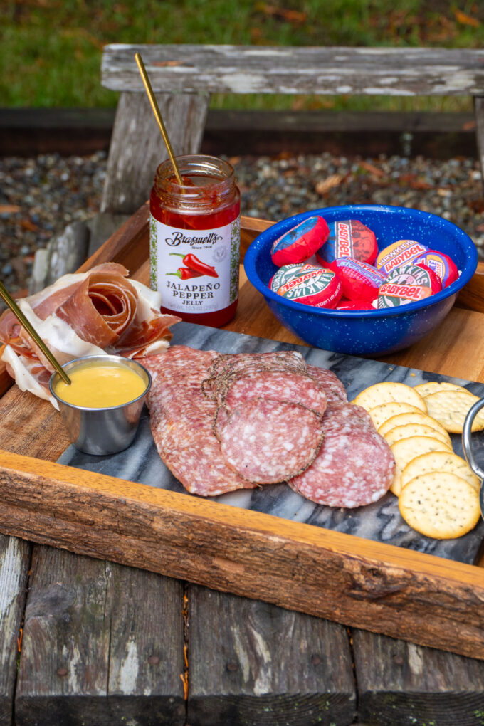 A close up of the charcuterie board with italian meat choices and a collectio onf sauces and jams sitting on an outdoor chair near the bonfire