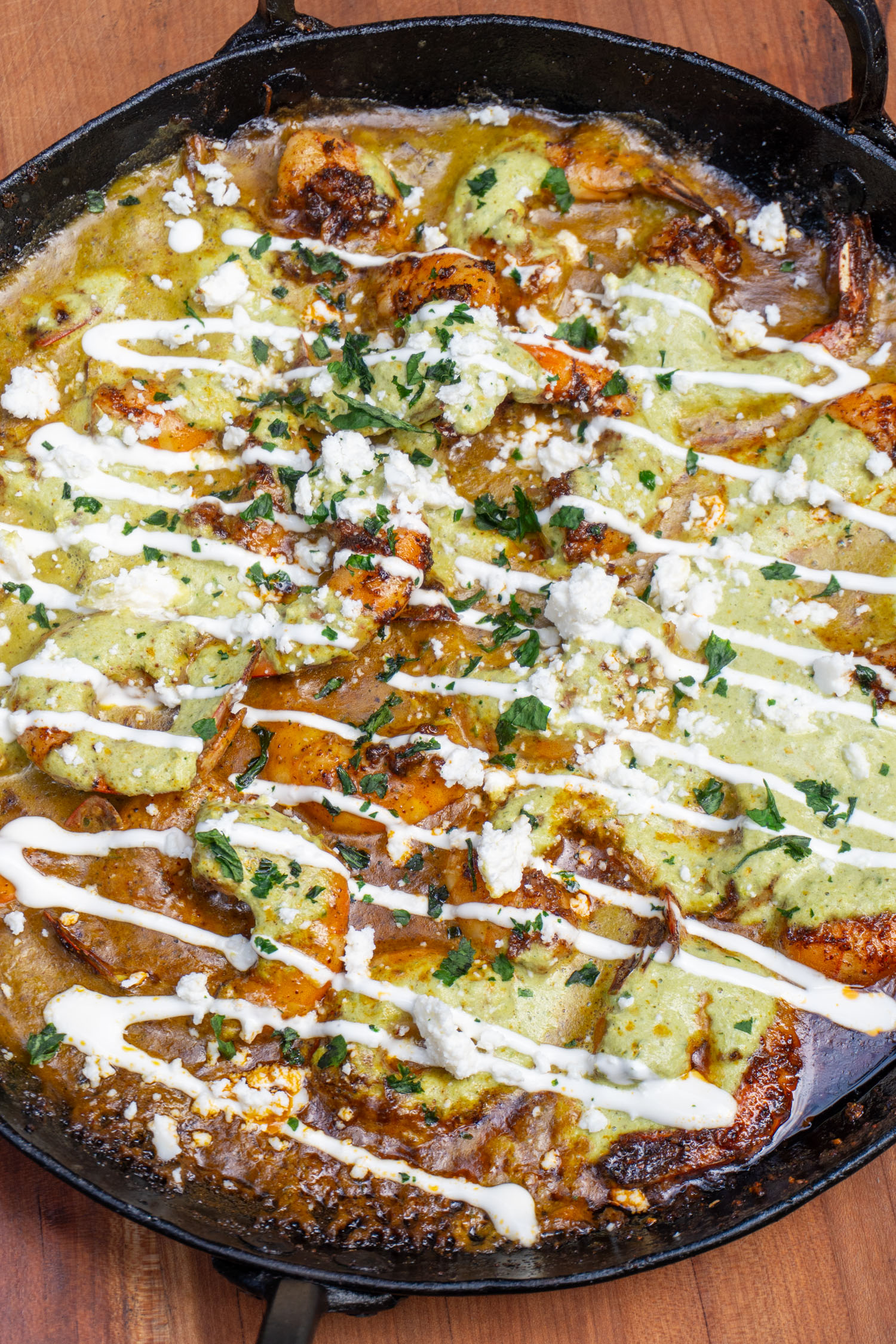 close up of poblano sauce poured over cooked garlic shrimp drizzled with crema