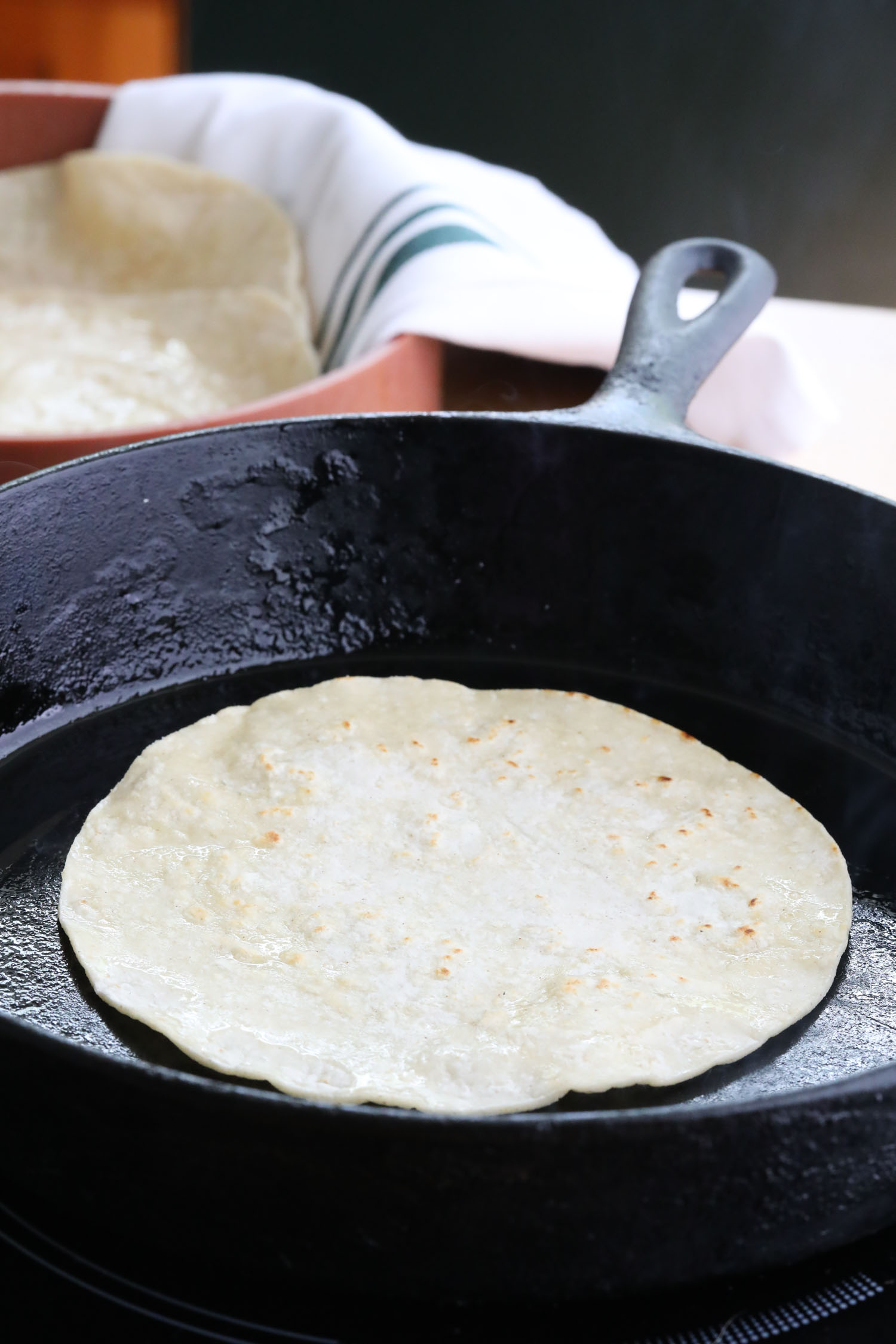 a cast iron skillet containing a corn tortilla frying in oil.