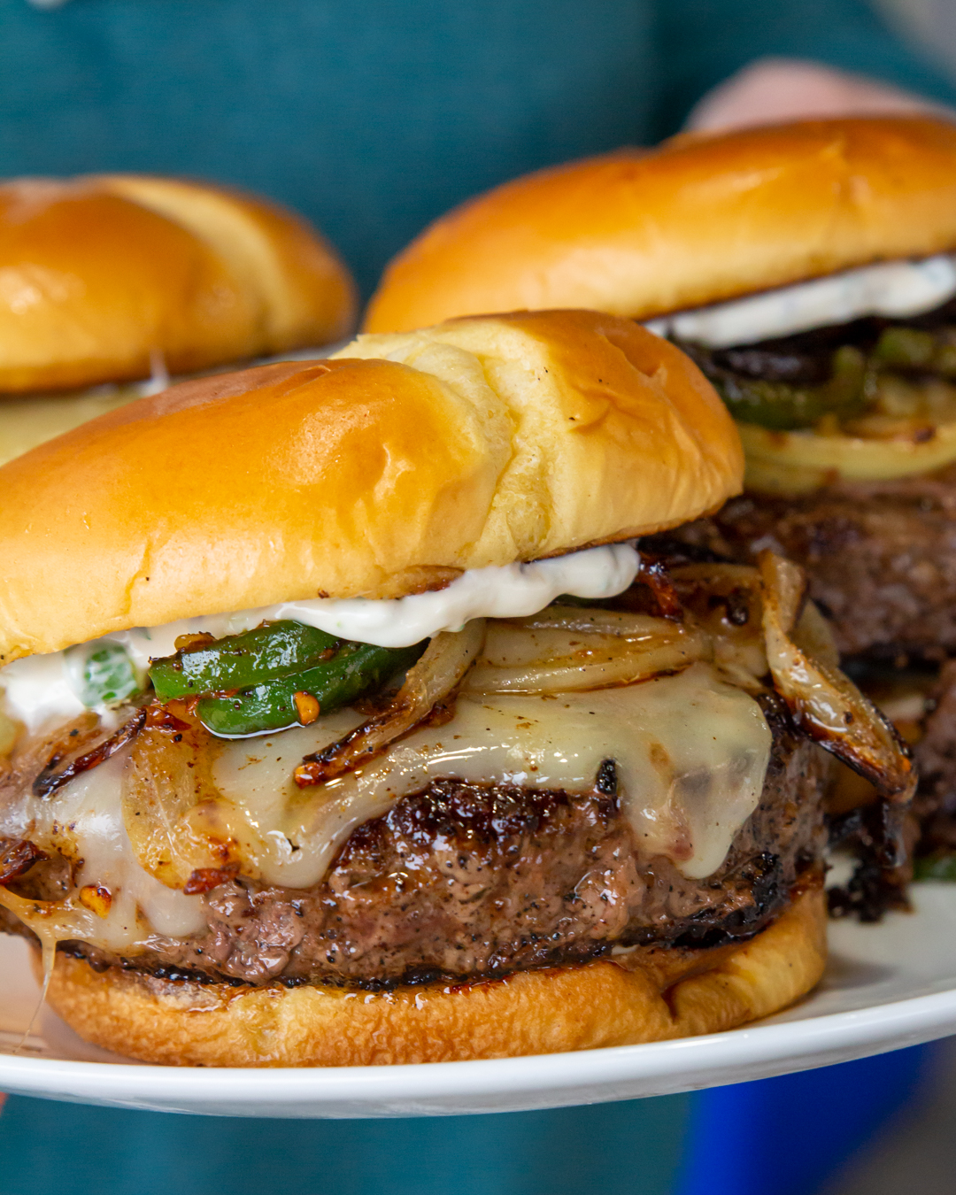 a plate of 3 juicy burgers on soft buns slathered with mayo, jalapenos, and griddled onion. 