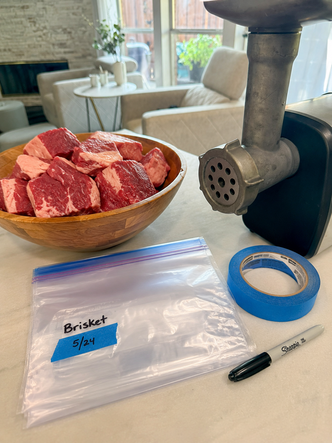 A meat grinder, bowl of brisket chunks, freezer bags, and labeling tools. 