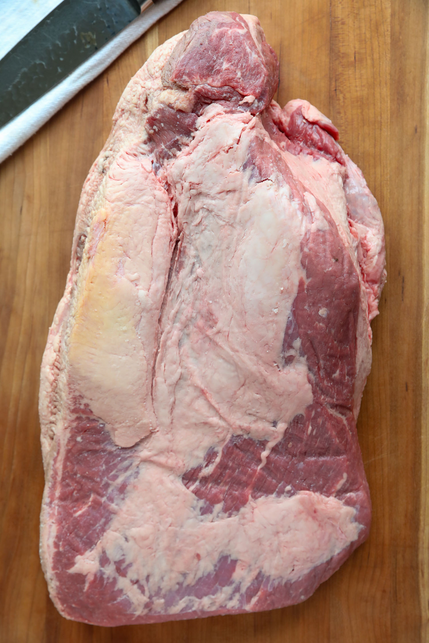 a whole beef brisket on a wooden cutting board